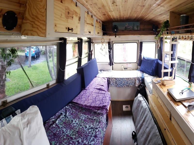 Budget skoolie conversion interior with plywood walls, seating area, and bed