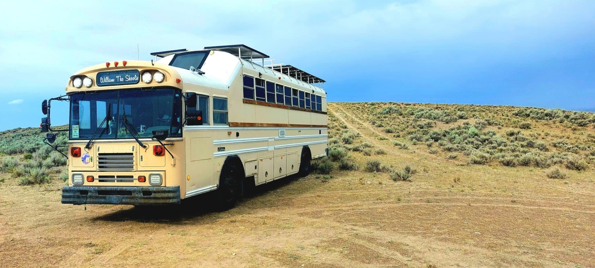 Converted school bus named William The Skoolie parked on open terrain with solar panels on the roof